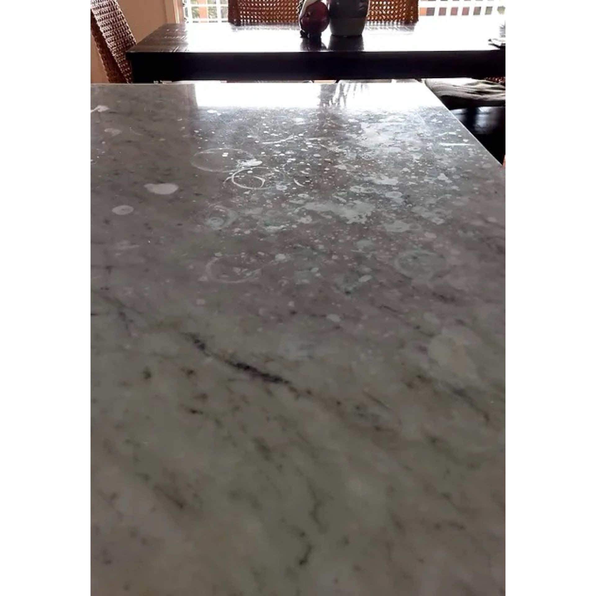 Close-up of a polished marble dining table surface with chairs in the background.